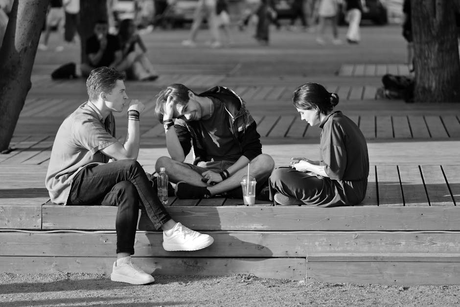Three young adults sitting on a bench chatting in a vibrant urban setting.